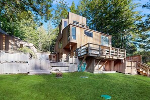 A modern wooden cabin with a multi-level deck, surrounded by a wooden fence and a grassy yard. - Sea Ranch 2BR Binker Barn with hot tub, yard & fire pit — dogs welcome (Sea Ranch)