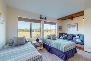 Un dormitorio con dos camas, un ventanal grande, un letrero en la pared que dice 'Playa' y un cuadro enmarcado.