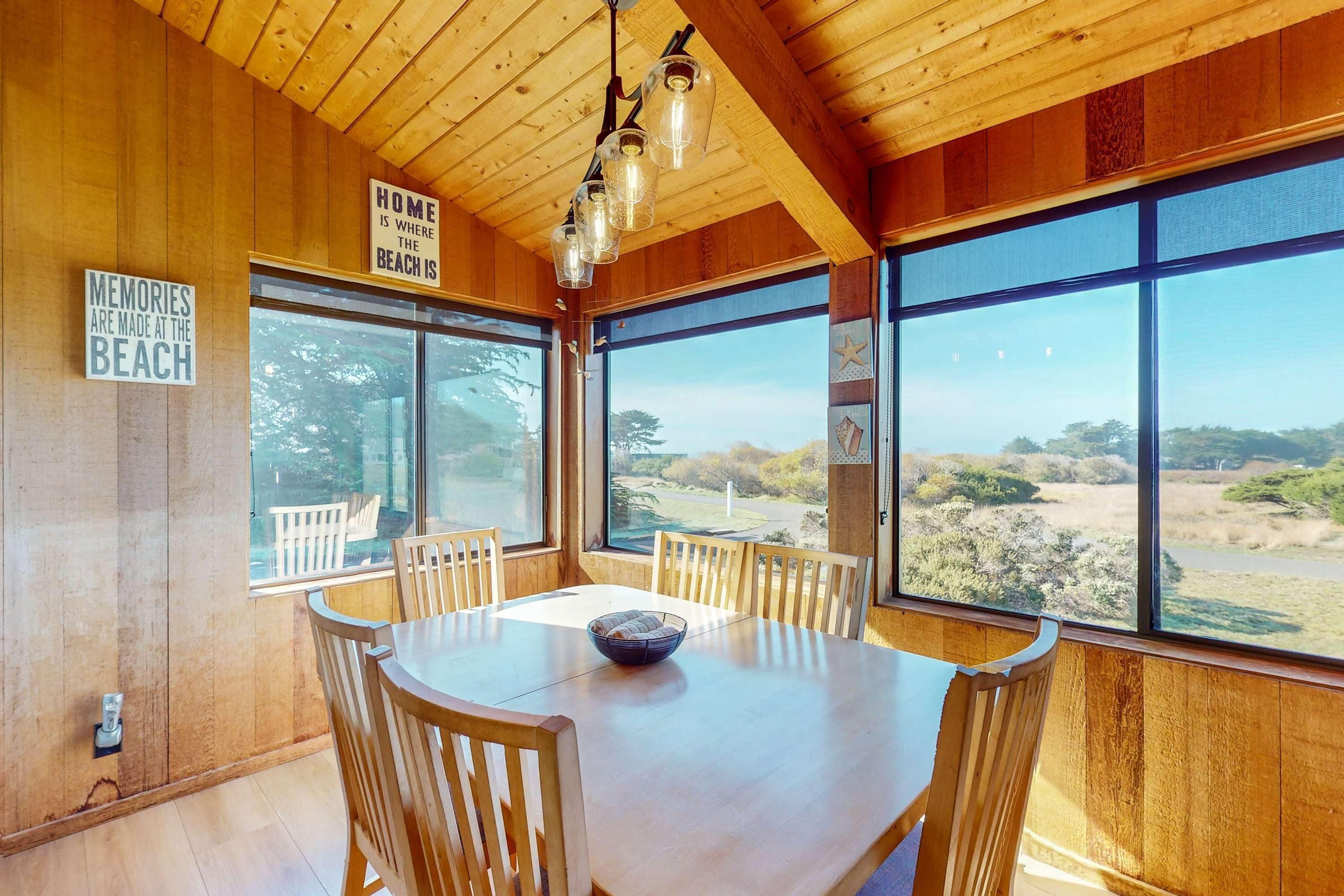 A wooden interior with a dining table, chairs, and large windows offering a view of the outdoors.