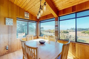 A wooden interior with a dining table, chairs, and large windows offering a view of the outdoors. - Sea Ranch 3BR dog-friendly home near playground & beach access (Sea Ranch)