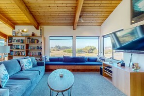 A modern living room with a wooden ceiling, large windows, a sofa, a coffee table, and a bookshelf. - Dog-Friendly Sea Ranch Home Near Playground & Beach (Sea Ranch)
