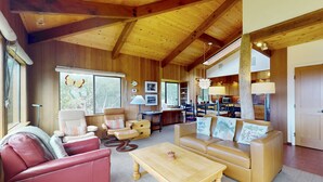Amplia sala de estar con techo de madera alta, sofás de cuero, mesa de centro de madera y vista al área de cocina y comedor.