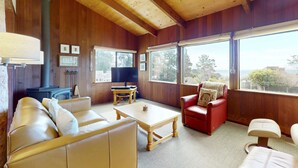 Una habitación acogedora con un sofá, una silla roja, una mesa de centro de madera, un televisor y un ventanal con vistas.