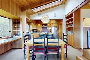 A modern kitchen with wooden cabinets, a central island, and a dining area with a table and chairs. - Classic Sea Ranch Home With Updated Amenities. Hot Tub. 1 Dog Allowed (Sea Ranch)