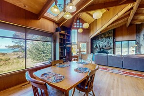 A wooden interior with a dining table, chairs, a bookshelf, and a stone fireplace. - Ocean-view home with hot tub near Black Point (Sea Ranch)