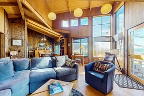 A cozy living room with a sectional sofa, a small armchair, and a coffee table. There are large windows offering a view of the outdoors. - Sea Ranch 3BR ocean-view home with private hot tub near Black Point (Sea Ranch)