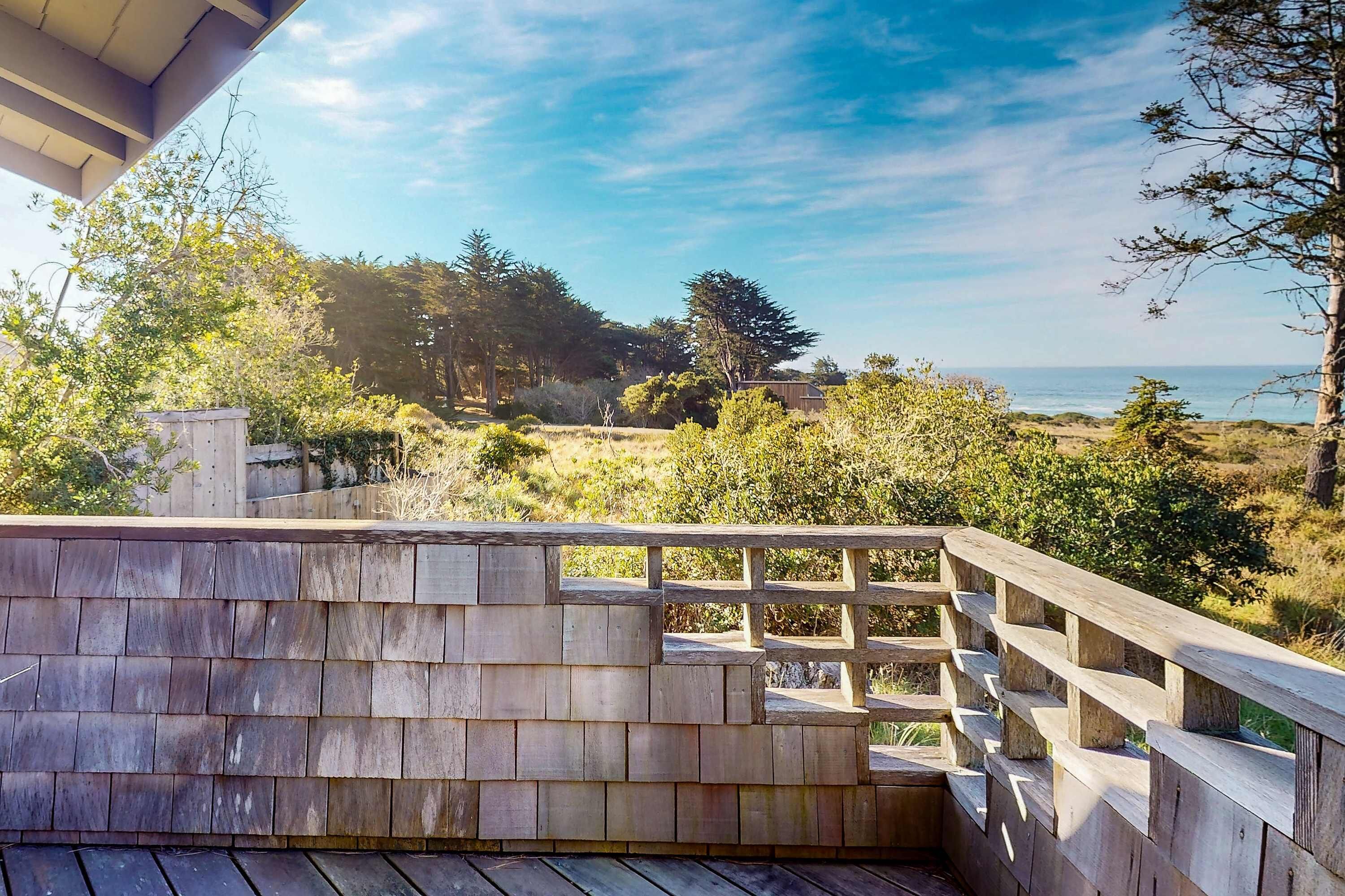 Un ponte di legno con ringhiera che si affaccia su un paesaggio naturale con alberi e vista sull'oceano.
