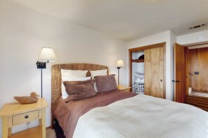 Un dormitorio con cama, dos lámparas de noche, cabecera de madera, armario de madera y una mesita con un adorno de pato.