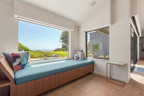A modern room with a built-in bench, large windows offering a view of the outdoors, and a small table. - Oceanfront home with fireplace, EV charger & ocean views (Sea Ranch)