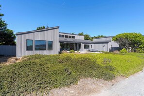 A modern two-story house with large windows and a well-maintained garden. - Oceanfront home with fireplace, EV charger & ocean views (Sea Ranch)