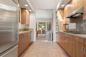 A modern kitchen with stainless steel appliances, wooden cabinets, and a view to the outdoors. - Oceanfront home with fireplace, EV charger & ocean views (Sea Ranch)