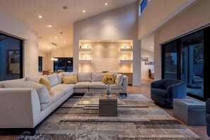 A modern living room with a sectional sofa, a coffee table, and a vase with flowers. - Oceanfront home with fireplace, EV charger & ocean views (Sea Ranch)