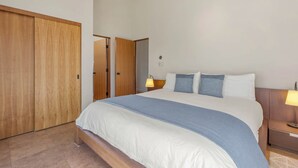 Ein Hotelzimmer mit einem großen Bett, zwei Nachttischlampen, einem Holzschrank und einer Tür zu einem anderen Raum.