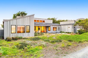 A modern two-story house with large windows, a covered patio, and a well-maintained garden. - Oceanfront home with fireplace, EV charger & ocean views (Sea Ranch)