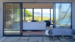 Ein Schlafzimmer mit einer großen Schiebeglaswand, die auf einen Balkon mit Meerblick führt.