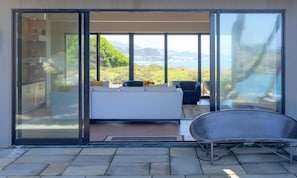 A bedroom with a large sliding glass door leading to a balcony with a view of the sea. - Oceanfront home with fireplace, EV charger & ocean views (Sea Ranch)
