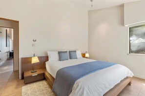 A bedroom with a bed, bedside lamps, a nightstand, a window with a view, and a door leading to another room. - Oceanfront home with fireplace, EV charger & ocean views (Sea Ranch)