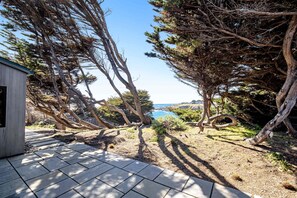 A patio with stone tiles, a wooden structure, and trees. - Oceanfront home with fireplace, EV charger & ocean views (Sea Ranch)