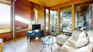 Una sala de estar moderna con un sofá, una mesa de centro de vidrio y un televisor sobre un mueble de madera.