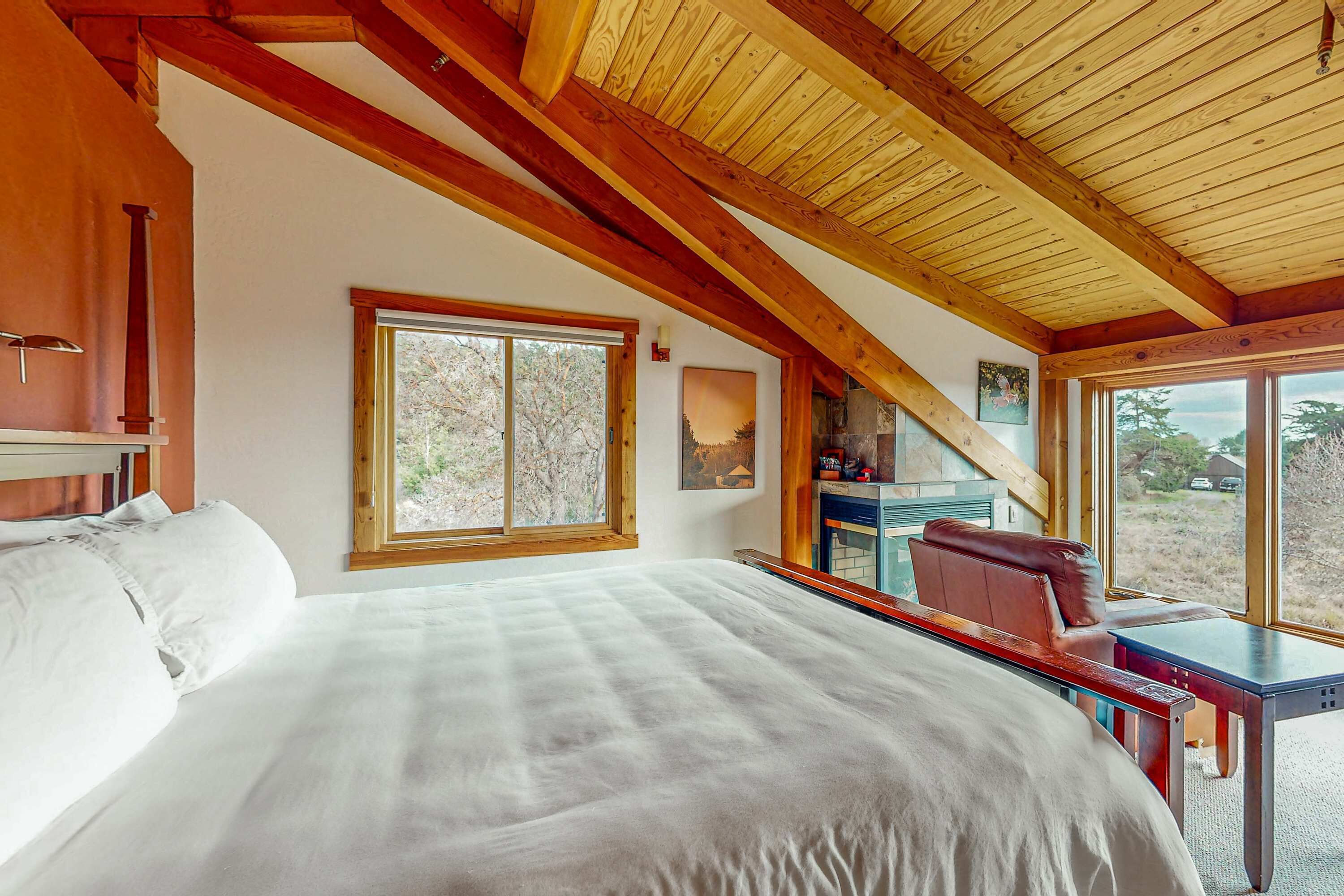A bedroom with a large bed, wooden beams, a desk, and a view of trees.