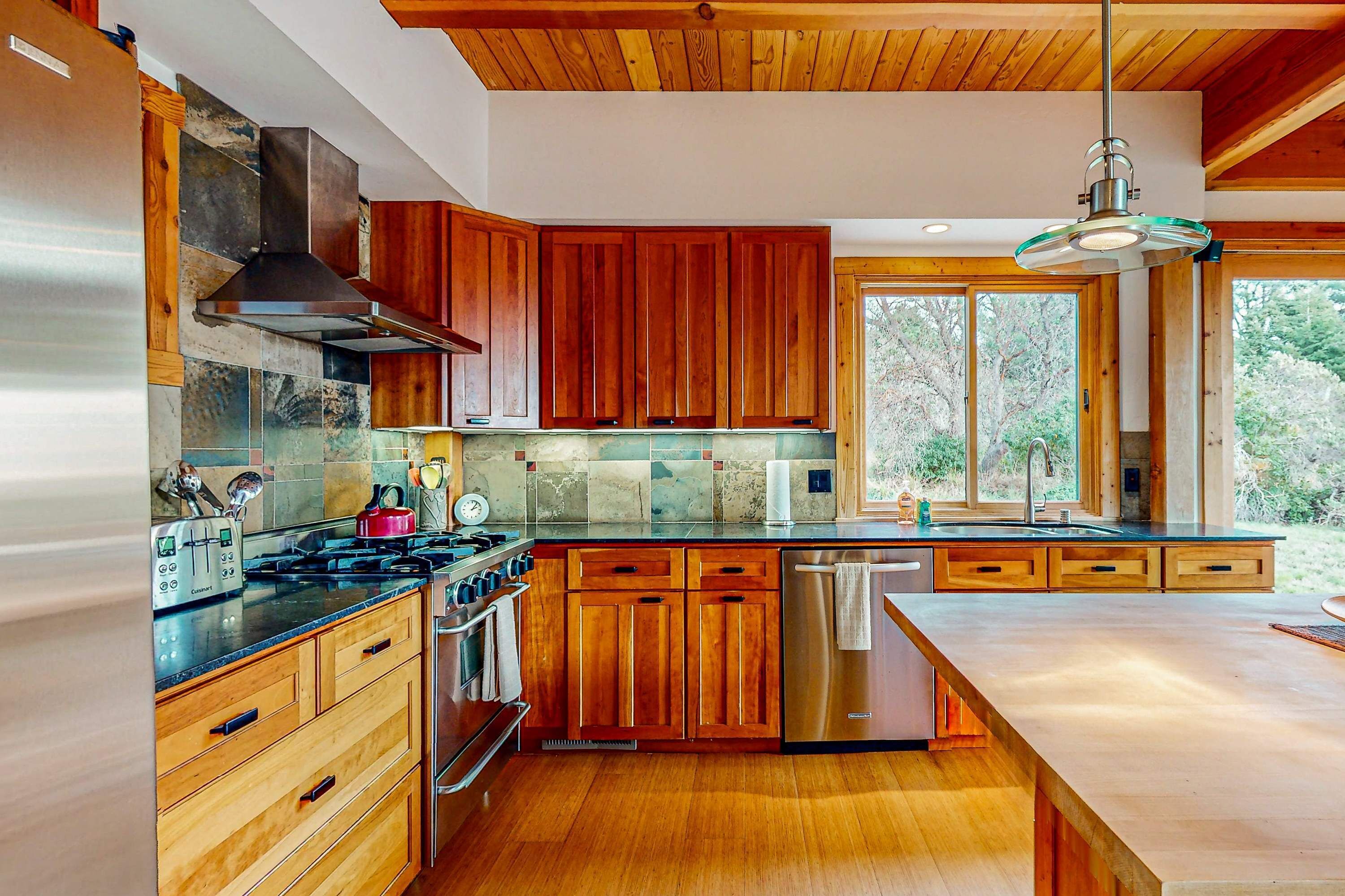 A modern kitchen with wooden cabinets, stainless steel appliances, and a large window.