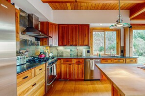 A modern kitchen with wooden cabinets, stainless steel appliances, and a large window. - Sea Ranch 3BR home, two decks & partial ocean views — dog welcome (Sea Ranch)