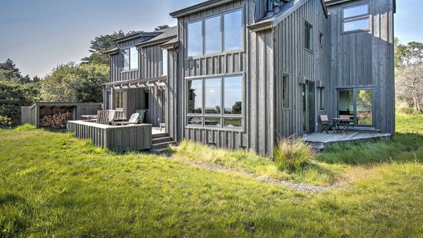 Ett modernt trähus med stora fönster, en veranda och utomhusmöbler.