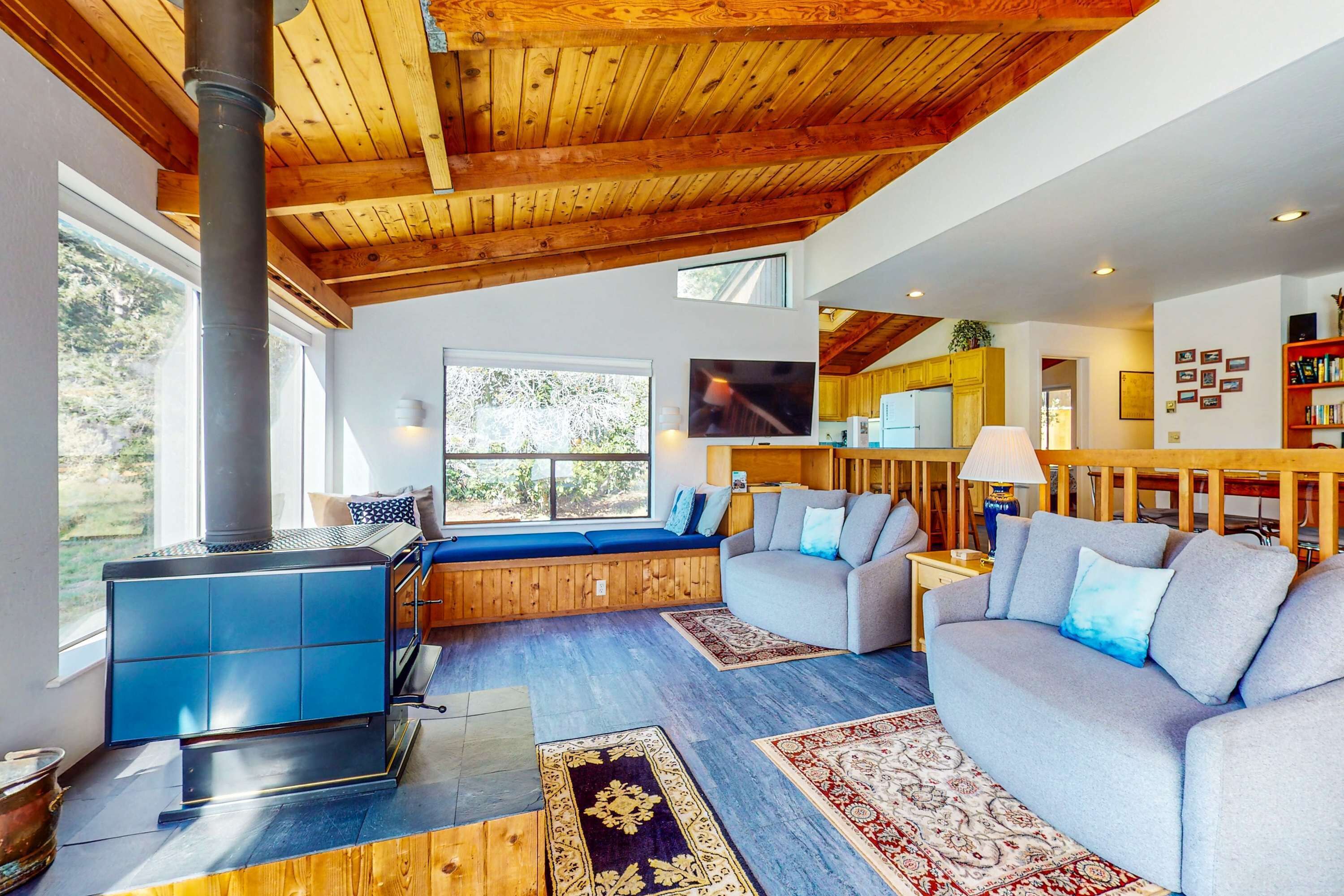 A cozy living room with a blue wood-burning stove, a grey sofa, and a wooden ceiling.