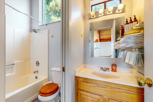 A bathroom with a bathtub, toilet, vanity with a sink, and a mirror with lights.