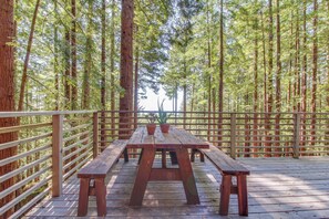 Une terrasse en bois avec des tables de pique-nique, entourée de grands arbres.