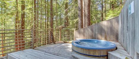 Eine Holzterrasse mit Whirlpool, umgeben von einem Holzzaun und hohen Bäumen.