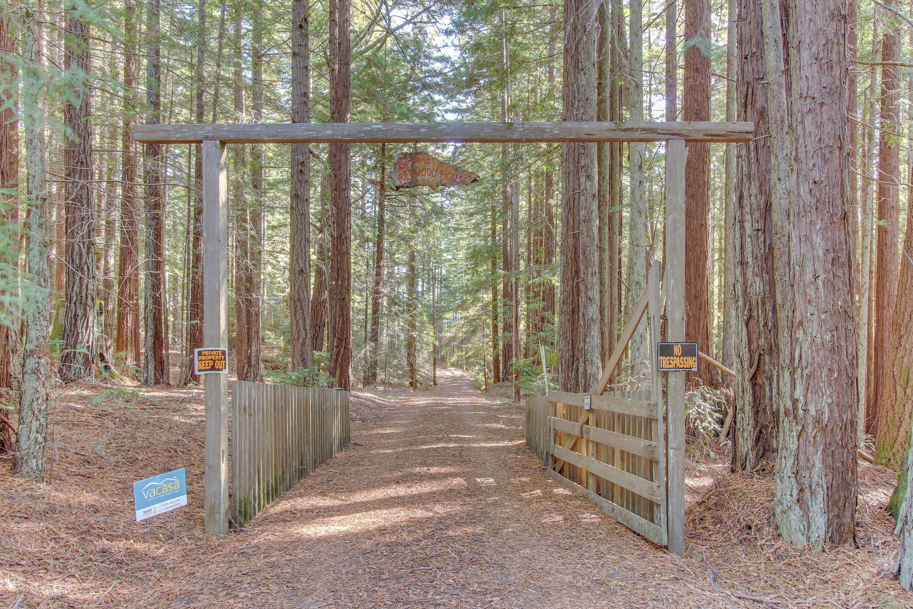 A forested area with a wooden gate, signs indicating a private property, and a path leading into the woods.