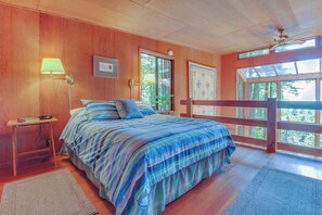 Une chambre à coucher avec un lit, des murs en bois, un ventilateur de plafond et de grandes fenêtres.