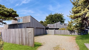 A modern building with a gravel driveway and wooden fences. - Sea Ranch 2BR ocean-view home near the golf course & Bluff Trail (Sea Ranch)