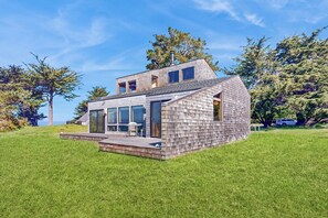 A modern two-story house with a deck, large windows, and a view of the surrounding trees. - Sea Ranch 2BR oceanfront home — meadow views near Black Point (Sea Ranch)
