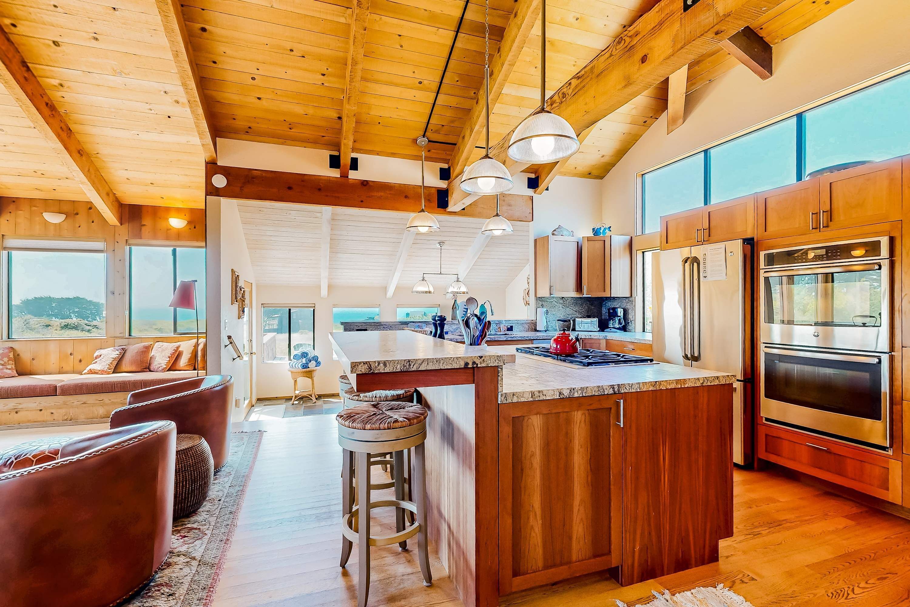 Une cuisine spacieuse avec des meubles en bois, un grand îlot central, des appareils électroménagers en acier inoxydable et une vue agréable par les fenêtres.