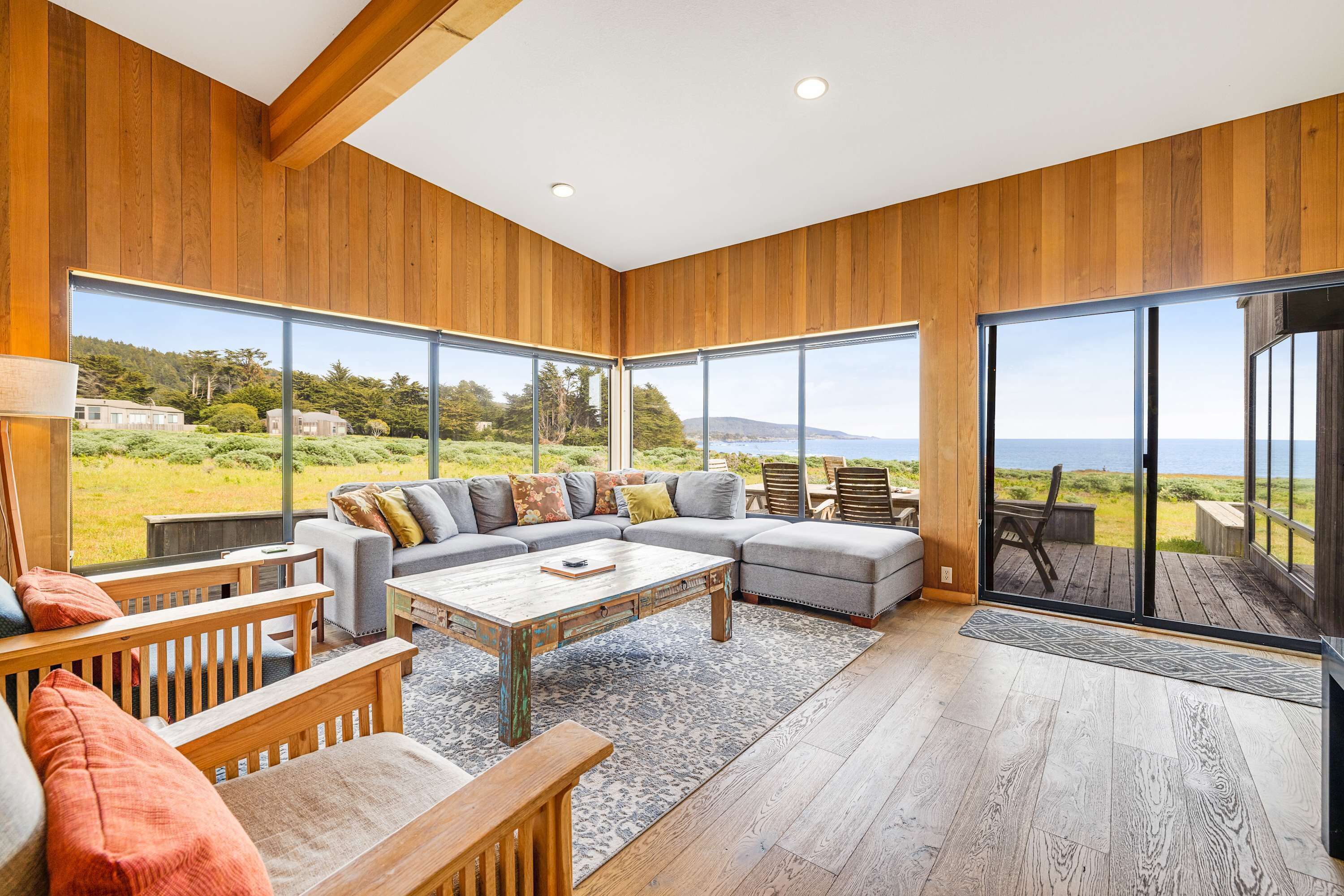 A modern living room with a sectional sofa, wooden flooring, large windows, and a view of the outdoors.