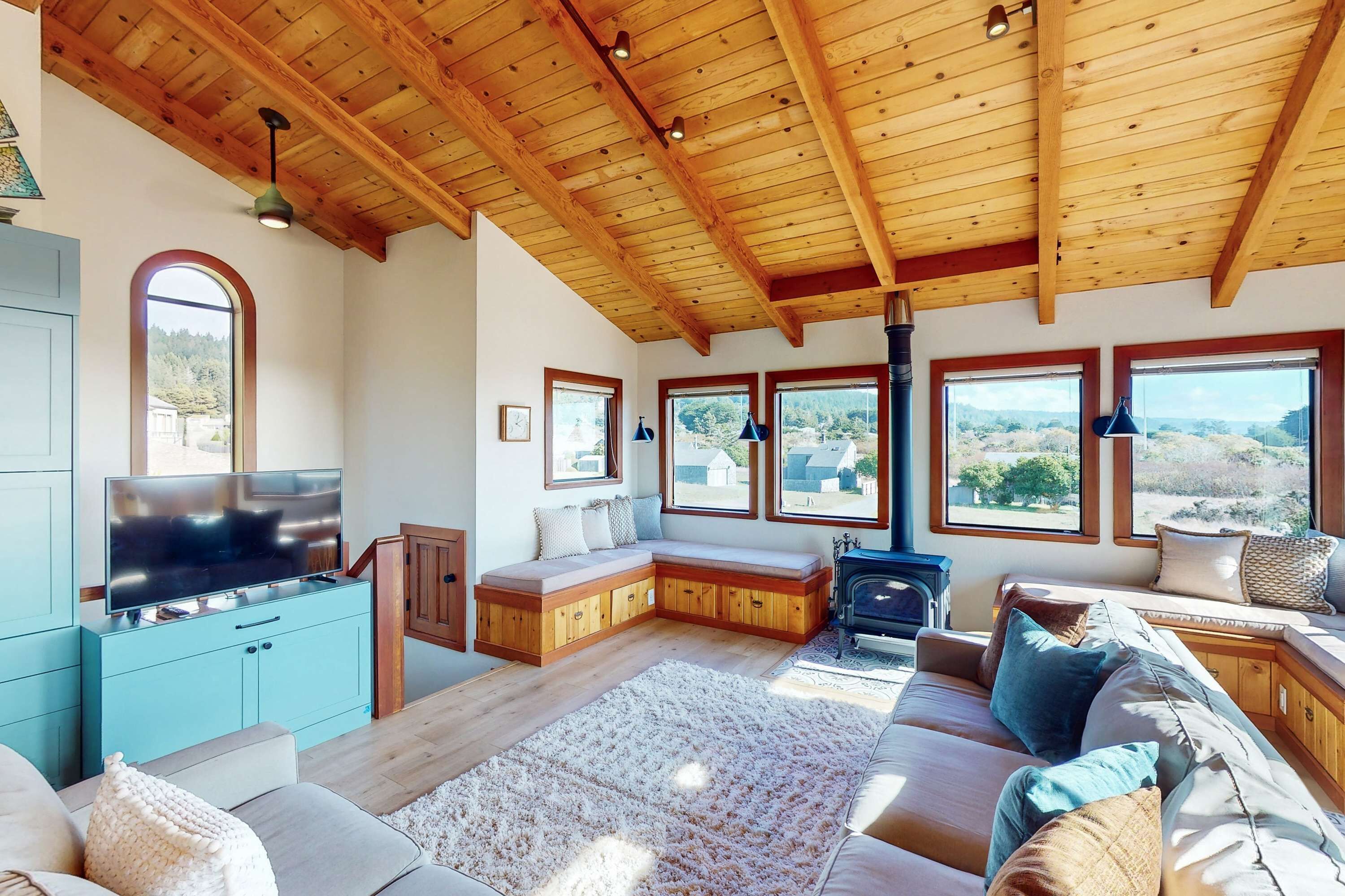 Amplia sala de estar con techo de madera, asientos integrados, televisor y grandes ventanas con vistas al exterior.