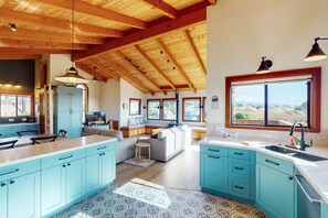 A spacious kitchen with blue cabinets, a large island, and a dining area with a sofa. - Sea Ranch 4BR home with hot tub & ocean views near Shell Beach (Sea Ranch)