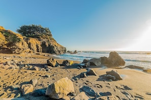 Ein felsiger Strand mit großen Steinen und einer Klippe, spärlich bewachsen.