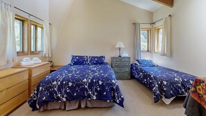 Quarto com duas camas, cómoda de madeira, mesa de cabeceira e janela com cortinas.