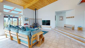 Uma sala de estar moderna com teto de madeira, um sofá grande, lareira e televisão.