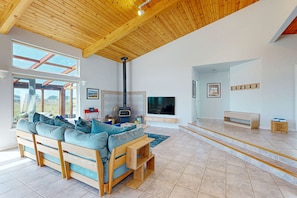 A modern living room with a wooden ceiling, a large sofa, a fireplace, and a TV. - Ocean-view blufftop home with courtyard on the meadow, dogs welcome (Sea Ranch)
