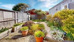 Um jardim com vasos de plantas, cerca de madeira e um edifício ao fundo.
