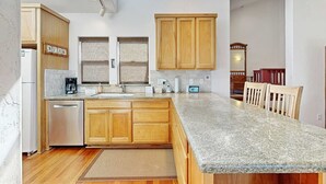 Una cocina con armarios de madera, encimeras de granito, lavavajillas integrado y un comedor con mesa y sillas de madera.