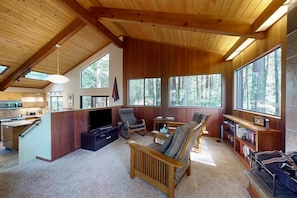 A spacious living area with a wooden ceiling, large windows, a kitchen, and a cozy seating area. - Sea Ranch 2BR award-winning redwood forest retreat on private acre (Sea Ranch)