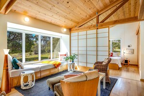 Ein modernes Interieur mit großem Fenster, einem Bett, einer Sitzecke und einer Holzbalkendecke.