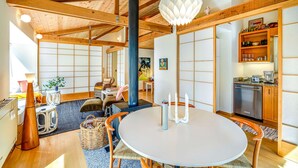 Et traditionelt japansk værelse med tatamigulv, et lavt tatami-bord, en sort søjle, en dekorativ hængende lampe og et tekøkken med træskabe og et køleskab.