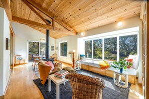 A spacious living area with a high ceiling, large windows, and a cozy seating arrangement. - Sea Ranch 1BR redwood cottage with private hot tub — dog friendly (Sea Ranch)