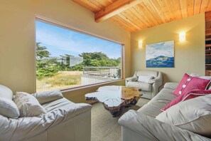 A room with a large window, a wooden ceiling, a painting on the wall, and a white sofa. - Sea Ranch 3BR meadow-view home with hot tub near golf course (Sea Ranch)
